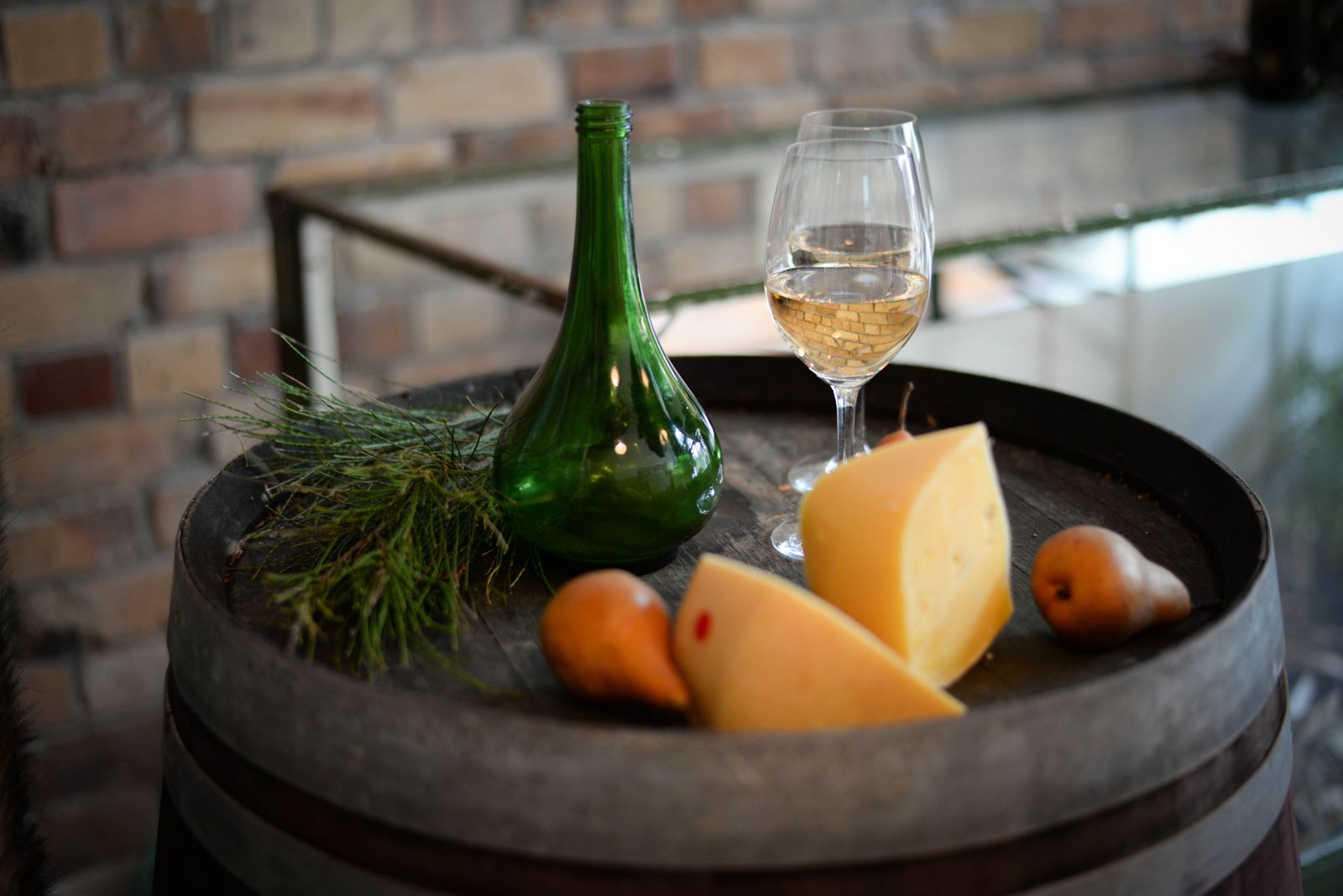 A barrel top with a green glass bottle, a glass of white wine, wedges of cheese and pears
