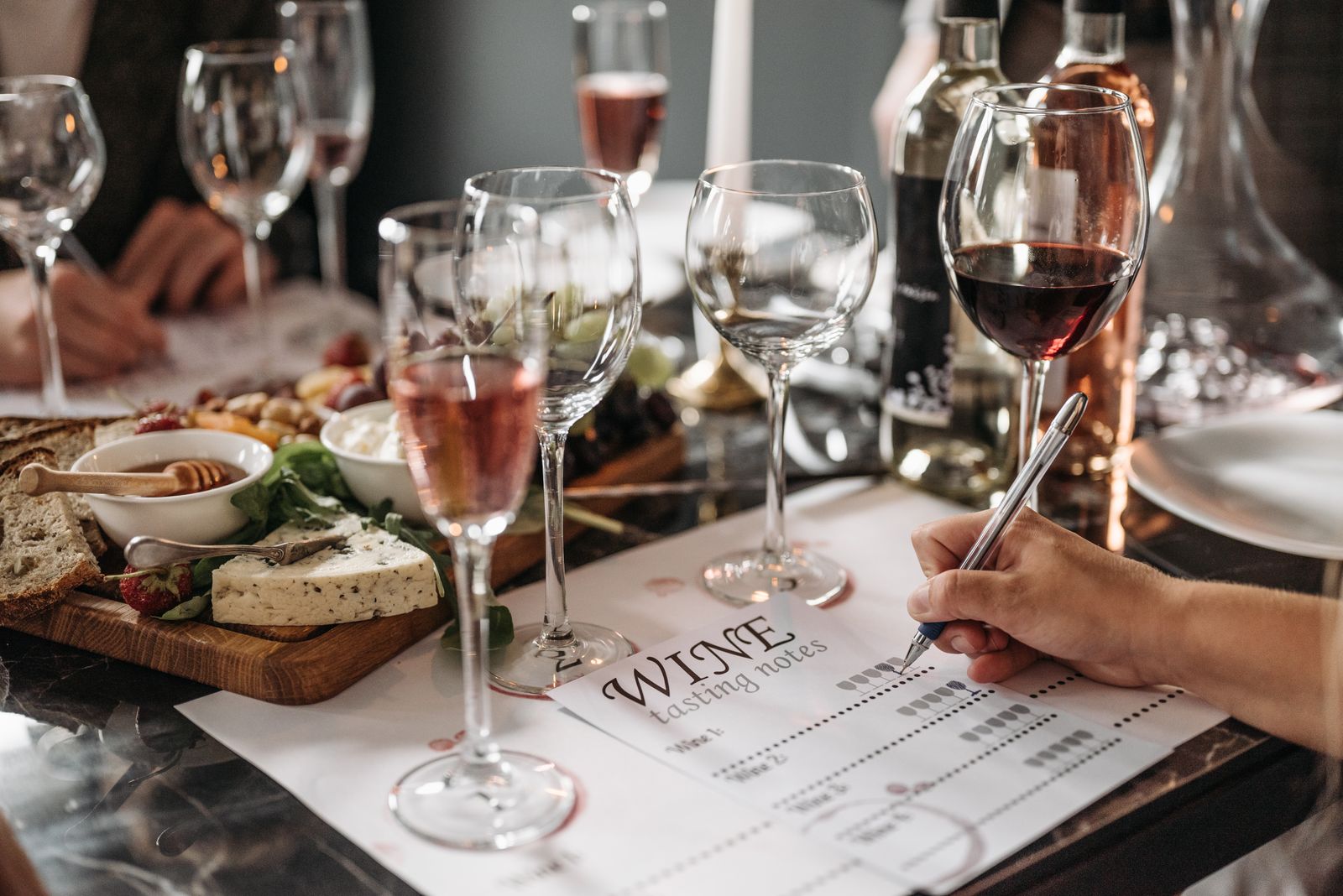 Wine glasses, a cheese and charcuterie board and a hand writing tasting notes at a table